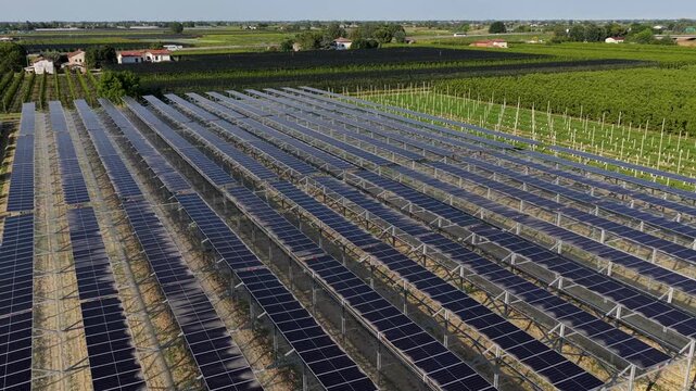 Aerial view of rows of solar panels installed over agricultural land under a clear blue sky in Faenza, Emilia-Romagna, Italy.