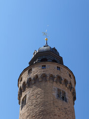 Low-angle view of the round upper section of Reichenbacher Tower in Goerlitz with historic masonry, stone corbels, tower roof and delicate weather vane against a blue sky. © Frank