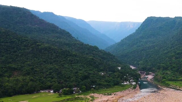 Mountain river flowing through the Khasi Hills landscape with indigenous village homes among the Meghalaya hill range near the India Bangladesh border - drone shot