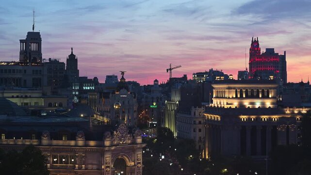 Panoramic high angle view captures illuminated historic Madrid skyline with red Telefonica building framing a colorful sunset sky at twilight, Spanish capital architecture b-roll footage.