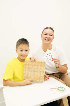 Child and teacher present a completed rubber band pattern on a wooden geoboard alongside the reference card after a hands-on geometry and spatial learning activity.