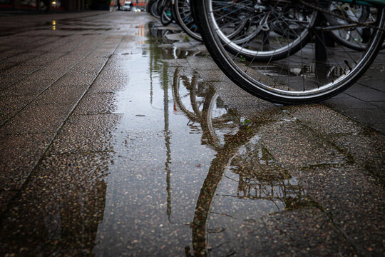Bicycle Wheels Reflected in Rain Puddles on an Urban Sidewalk