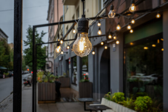 Glowing String Light Bulb Outside an Urban Cafe After Rain