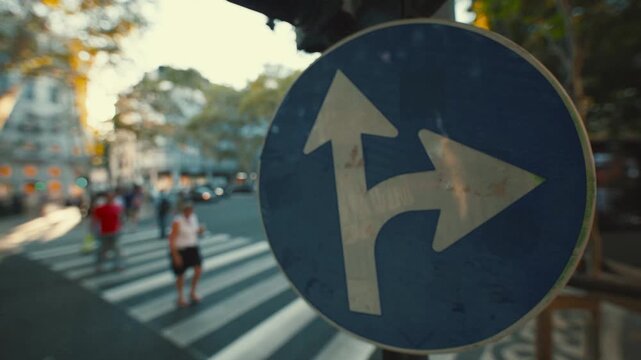 Traffic sign shows direction to continue straight or turn left in busy street in city during daytime