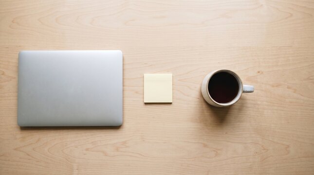 Modern workspace flat lay featuring closed silver laptop yellow sticky note coffee