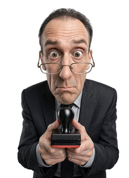 Middle-aged man looks surprised while holding a rubber stamp toward camera. He wears glasses and a dark suit against a plain white background.