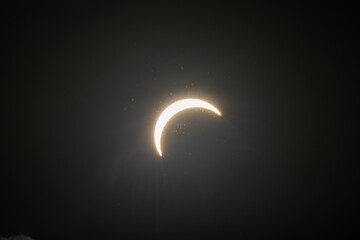Partial solar eclipse captured as the Moon passes in front of the Sun, creating a striking crescent shape against the dark sky. An astronomical event photographed during daylight. © KjLOWRYPHOTOGRAPHY