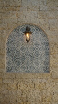 Vintage brass wall lantern mounted on a decorative blue tile niche in a textured stone wall.