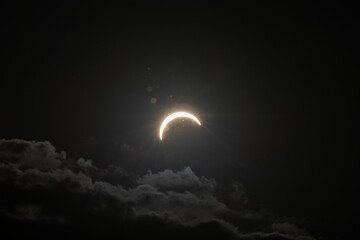 Partial solar eclipse captured as the Moon passes in front of the Sun, creating a striking crescent shape against the dark sky. An astronomical event photographed during daylight. © KjLOWRYPHOTOGRAPHY