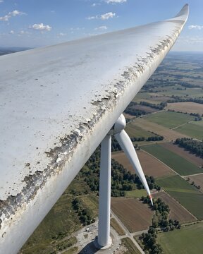 Drone inspection view reveals realistic leading-edge erosion on a wind turbine blade high above farmland.
