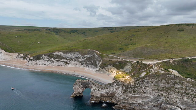 Aerial view of Durdle Door, a natural limestone arch on the Jurassic Coast, featuring rugged cliffs, a sandy beach, and calm blue sea in Wareham, England, United Kingdom.