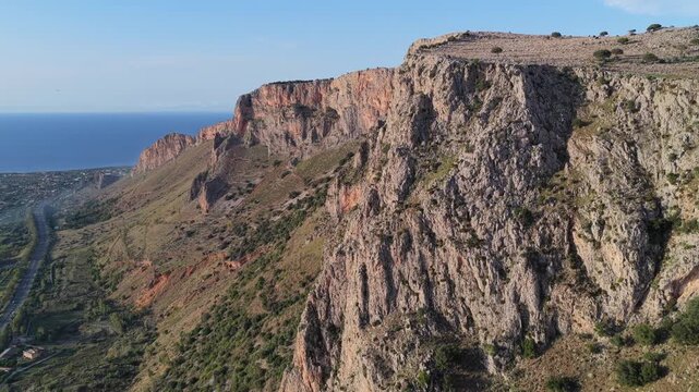 Aerial view of rugged rocky cliffs overlooking the Mediterranean Sea with coastal vegetation and a road in Terrasini, Sicily, Italy.