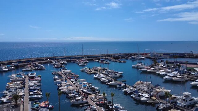 Dron se eleva sobre un aparcamiento y revela el puerto deportivo de Puerto Col&oacute;n lleno de yates y lanchas amarradas, Costa Adeje, Tenerife, Islas Canarias, Espa&ntilde;a