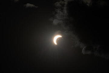 Partial solar eclipse captured as the Moon passes in front of the Sun, creating a striking crescent shape against the dark sky. An astronomical event photographed during daylight. © KjLOWRYPHOTOGRAPHY