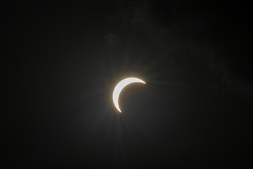 Partial solar eclipse captured as the Moon passes in front of the Sun, creating a striking crescent shape against the dark sky. An astronomical event photographed during daylight. © KjLOWRYPHOTOGRAPHY