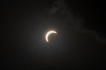 Partial solar eclipse captured as the Moon passes in front of the Sun, creating a striking crescent shape against the dark sky. An astronomical event photographed during daylight. © KjLOWRYPHOTOGRAPHY