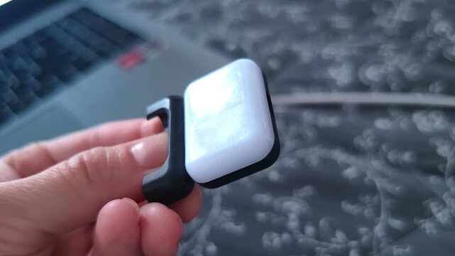 Hand demonstrates a compact LED phone light from the side, showing its illuminated panel and mounting mechanism, portable photography and video equipment.