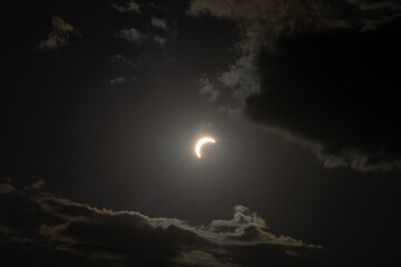 Partial solar eclipse captured as the Moon passes in front of the Sun, creating a striking crescent shape against the dark sky. An astronomical event photographed during daylight. © KjLOWRYPHOTOGRAPHY