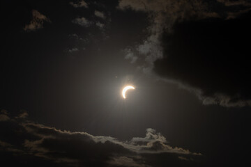 Partial solar eclipse captured as the Moon passes in front of the Sun, creating a striking crescent shape against the dark sky. An astronomical event photographed during daylight. © KjLOWRYPHOTOGRAPHY