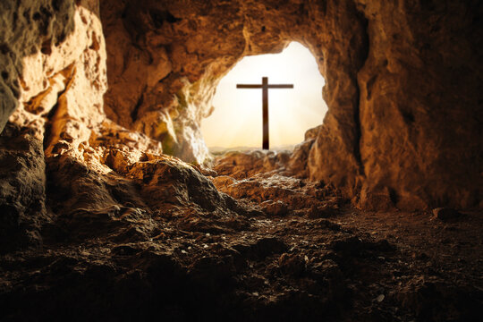Silhouette of cross seen through rocky cave opening at sunrise, Easter resurrection religious concept