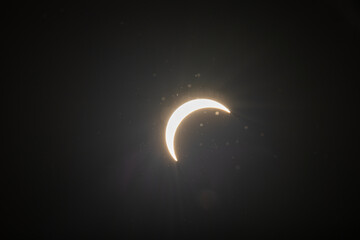 Partial solar eclipse captured as the Moon passes in front of the Sun, creating a striking crescent shape against the dark sky. An astronomical event photographed during daylight. © KjLOWRYPHOTOGRAPHY