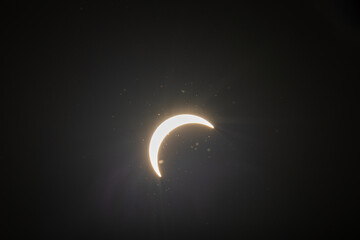 Partial solar eclipse captured as the Moon passes in front of the Sun, creating a striking crescent shape against the dark sky. An astronomical event photographed during daylight. © KjLOWRYPHOTOGRAPHY