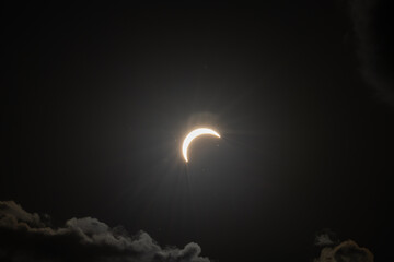 Partial solar eclipse captured as the Moon passes in front of the Sun, creating a striking crescent shape against the dark sky. An astronomical event photographed during daylight. © KjLOWRYPHOTOGRAPHY