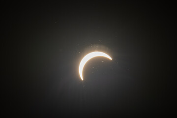 Partial solar eclipse captured as the Moon passes in front of the Sun, creating a striking crescent shape against the dark sky. An astronomical event photographed during daylight. © KjLOWRYPHOTOGRAPHY