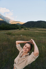 Obraz premium A smiling woman enjoys outdoor lifestyle in a field with distant mountains, capturing a carefree moment in nature in a sunlit meadow, wearing casual attire.
