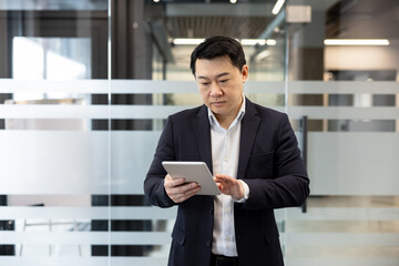Businessman using a tablet in a modern office for financial analysis and business management. Professional man checking digital documents on a mobile device to improve corporate communication. © Liubomir