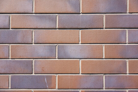 Textured brown brick wall with horizontal and vertical alignment, showcasing various shades and subtle imperfections in the surface