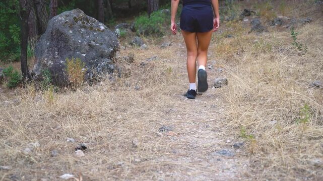 Close-up of woman's legs in sneakers walking on a dirt forest trail. Outdoor fitness trekking and active walking concept
