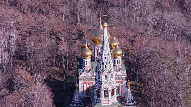 Aerial view of the Shipka Memorial Church with its golden domes and intricate architecture surrounded by a dense forest in Shipka, Stara Zagora, Bulgaria.