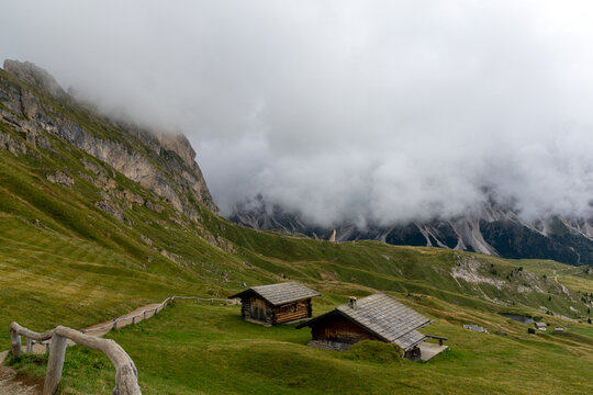 Sankt Ulrich, Italy - August 25, 2026: Wooden alpine huts below a fog-shrouded cliff in the Dolomites