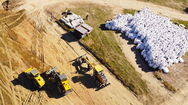 An elevated aerial drone photograph capturing yellow construction machinery, including a road roller, wheel loader, and motor grader, parked at an active development site.