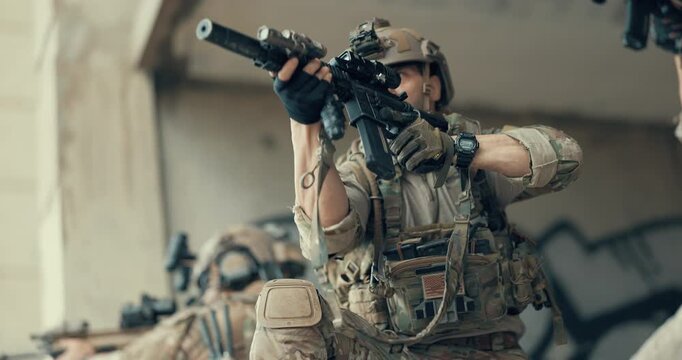 Close up of military tactical operator aiming suppressed rifle in abandoned building