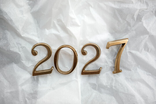 Gold metal numbers spelling 2027 lie on crumpled white tissue paper, symbolizing the new year, fresh start, celebration, future planning and goals for the coming year in a minimalist styled photo.
