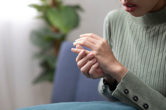 A young woman is experiencing pain in her hands and fingers and is trying to relieve the discomfort by massaging them gently.