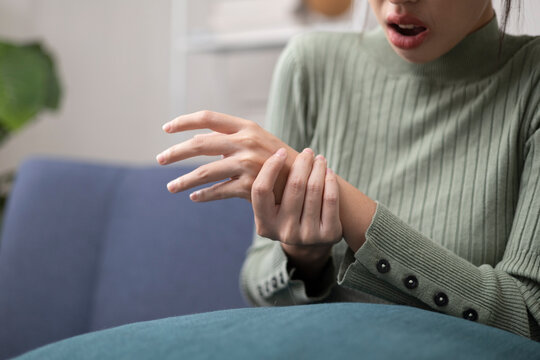 A young woman is experiencing pain in her hands and fingers and is trying to relieve the discomfort by massaging them gently.