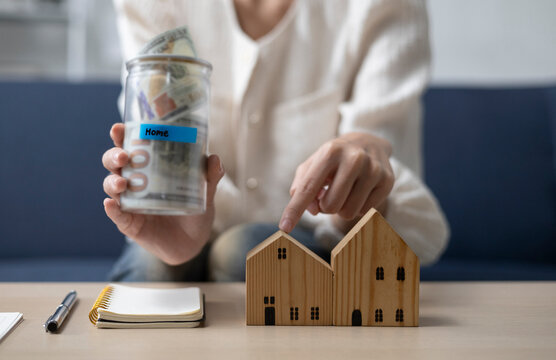 A young woman is sitting and shopping for a house using money she saved in a piggy bank, while noting down expenses and keeping track of her finances.