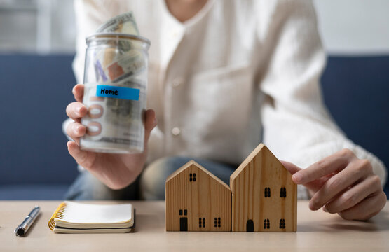 A young woman is sitting and shopping for a house using money she saved in a piggy bank, while noting down expenses and keeping track of her finances.