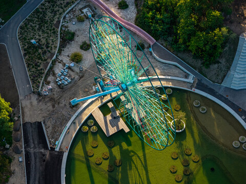 Aerial view of the iconic Ferris wheel at Spreepark in Berlin, surrounded by lush green parkland, pathways, and shadows cast during the golden hour in Berlin, Berlin, Germany.
