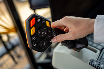 Operator hand holding multifunctional control joystick with buttons inside modern agricultural tractor or combine harvester cabin. © Marina