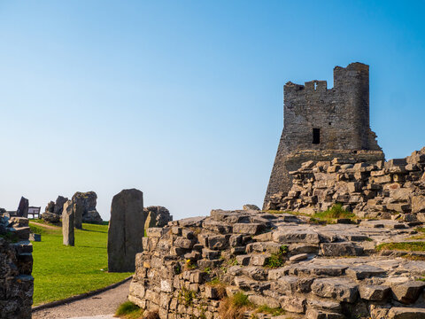 Aberystwyth Castle, with wall and standing stones situated on a grassy hillside with a clear sky and a path leading to it.