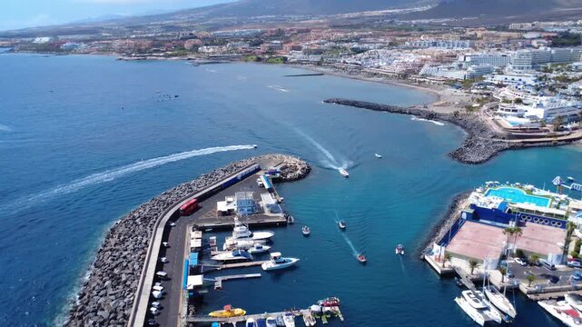 Vista a&eacute;rea de la entrada del puerto de Puerto Col&oacute;n con barcos saliendo al mar y la costa tur&iacute;stica de Costa Adeje al fondo, Tenerife, Islas Canarias