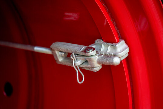 Metal dual wheel clamp latch mechanism with cotter pin installed on red rim flange of heavy agricultural machinery.
