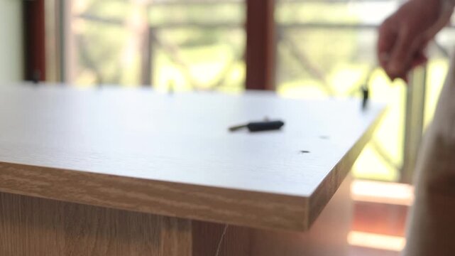 Extreme close up of male hand screwing metal fastener pin into wooden board for DIY desk assembly, handyman assembling wooden furniture at home