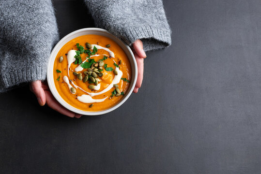 Female hands in knitted sweater holding bowl with pumpkin soup