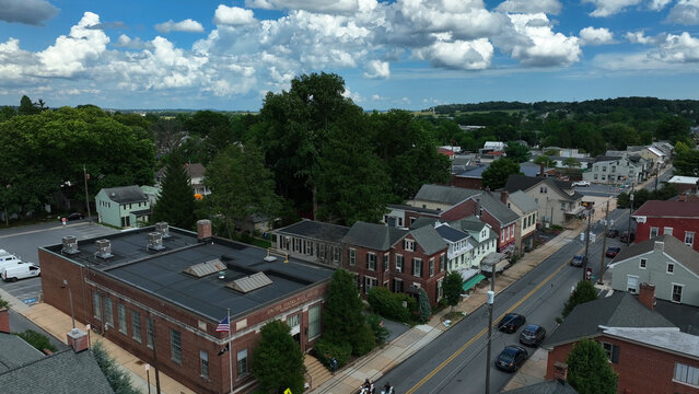 Aerial view of the United States Post Office building surrounded by historic brick houses, lush green trees, and a quiet street in Manheim, Pennsylvania, United States.