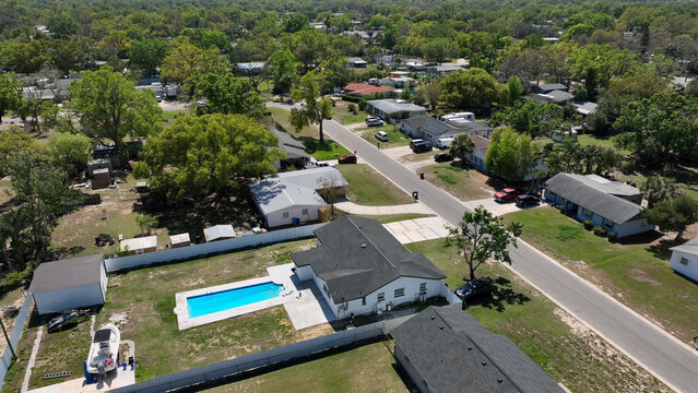 Aerial view of a residential neighborhood featuring single-family homes, a backyard swimming pool, lush green trees, and paved streets in Brandon, Florida, United States.
